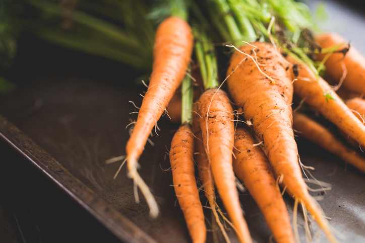 A bunch of fresh orange carrots with tops, one of the common mirepoix vegetables.